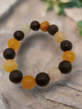 A stretch bracelet featuring black lava and yellow jade beads, displayed on a wooden surface.