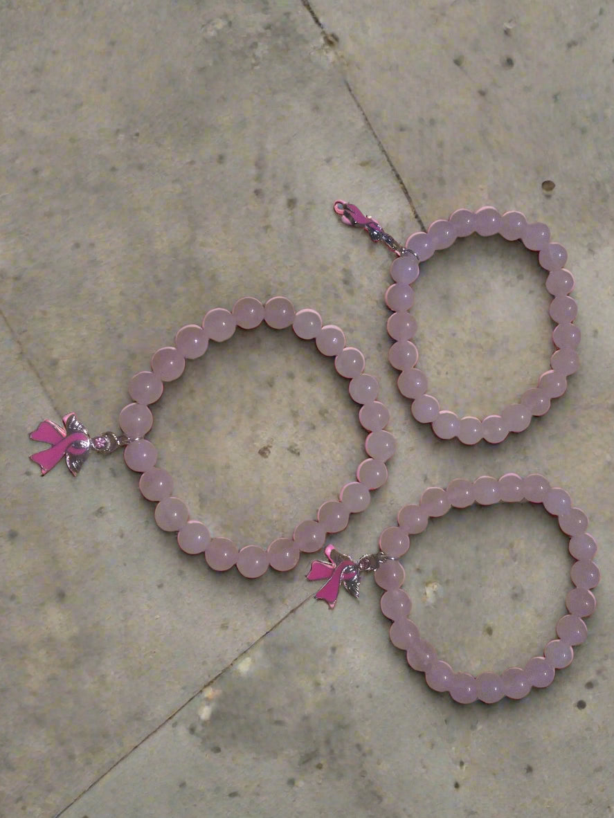 Three pink beaded bracelets with breast cancer awareness charms on a street surface.