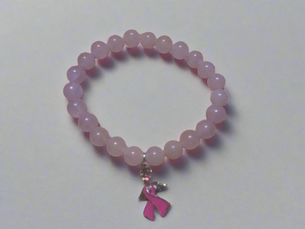 Rose quartz beaded stretch bracelet with silver angel charm featuring a pink breast cancer awareness ribbon, displayed on a wooden background.