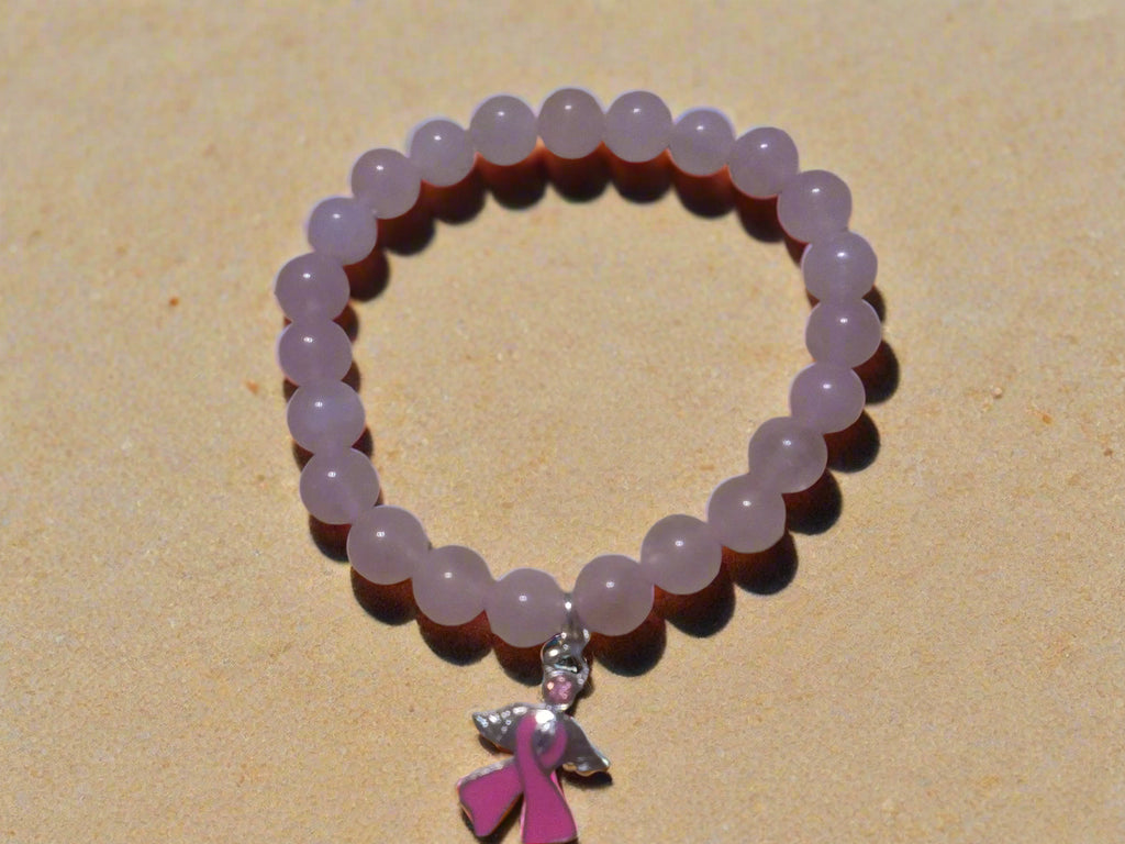 Pink beaded bracelet with a pink ribbon charm on a sandy surface