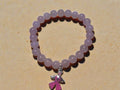 Pink beaded bracelet with a pink ribbon charm on a sandy surface
