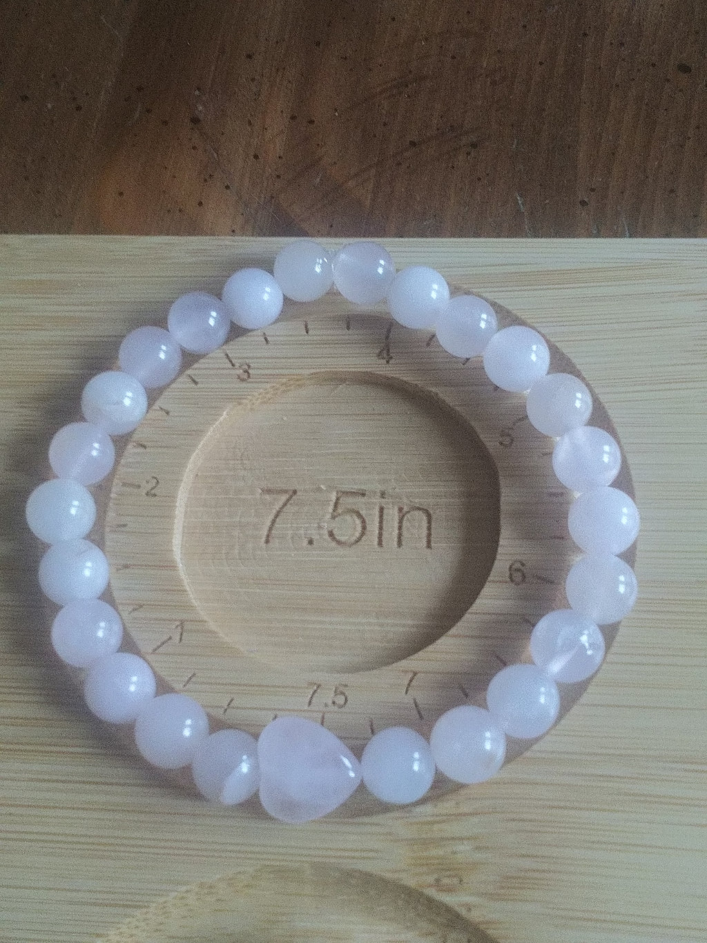 Pink beaded bracelet on a wooden board with measurement markings