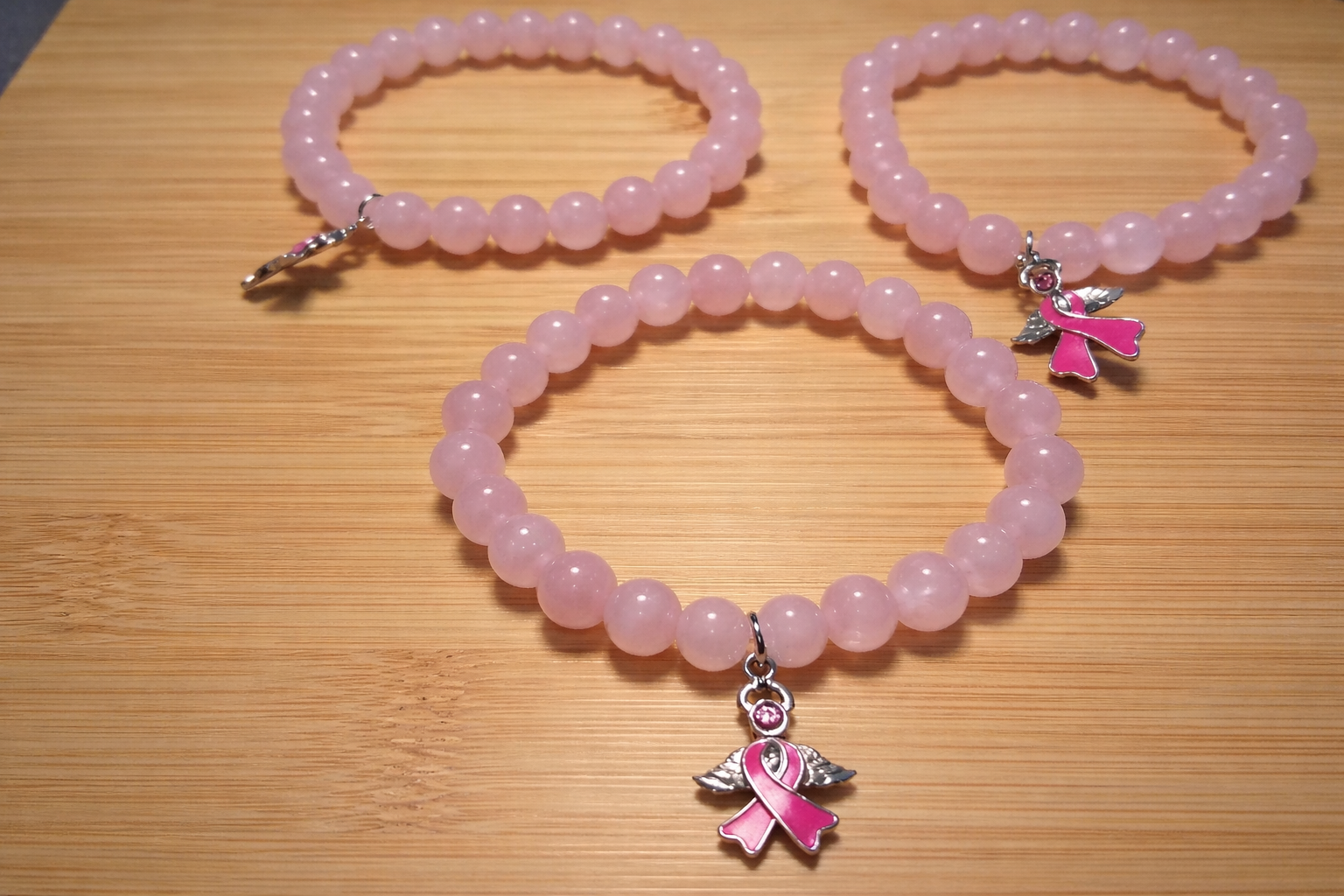 Three pink beaded bracelets with angel charms on a wooden surface