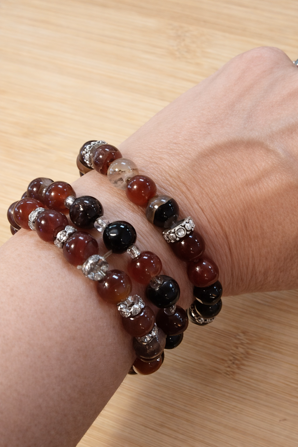 Close-up of a wrist wearing three beaded bracelets on a wooden surface