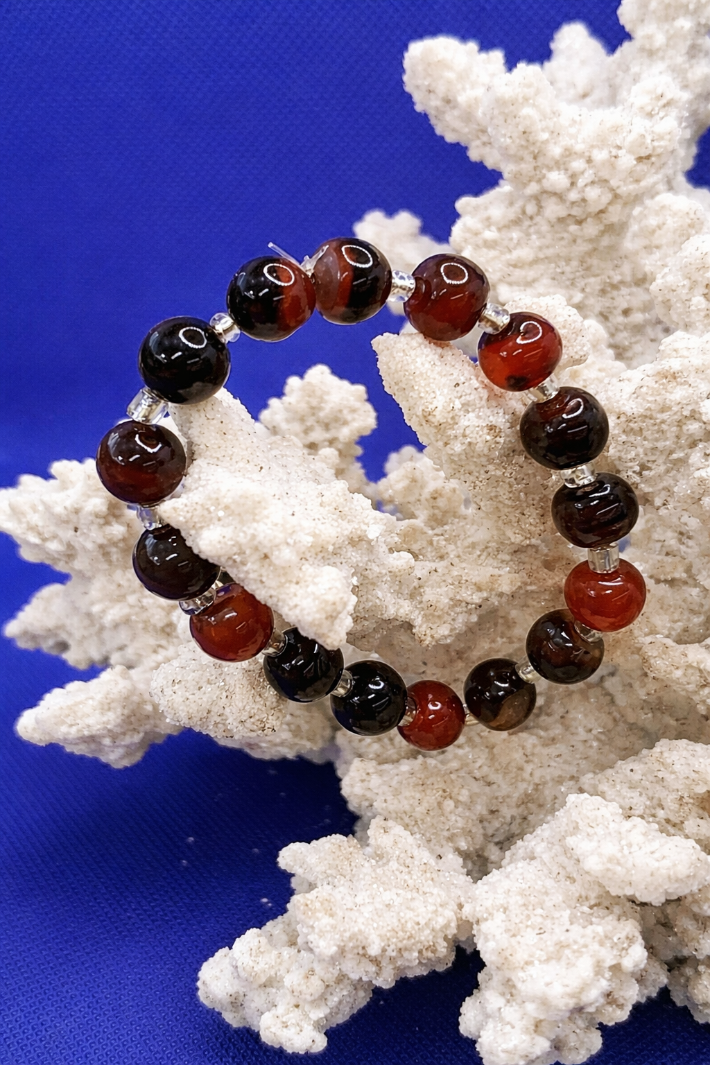 Bracelet with red and black beads on a white coral structure against a blue background