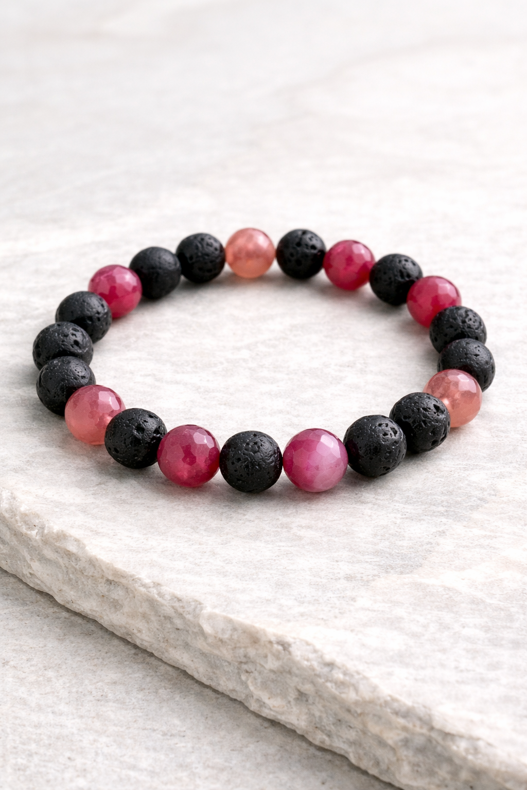 Bracelet with black and pink beads on a light stone surface
