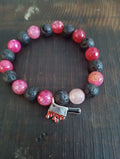 Bracelet with red agate and black lava beads and a silver charm on a dark surface