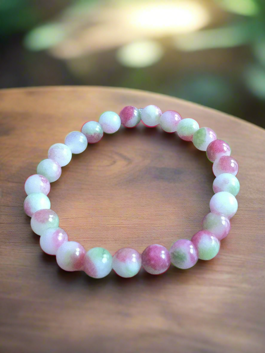 Watermelon tourmaline beaded bracelet on a wooden surface with a blurred natural background