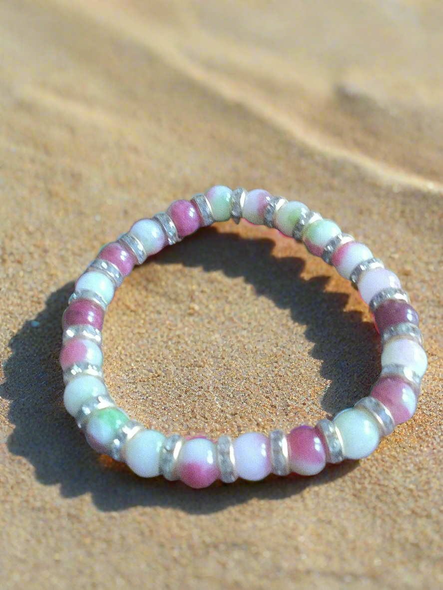 Beaded bracelet with pink, green, and white beads on a sandy background